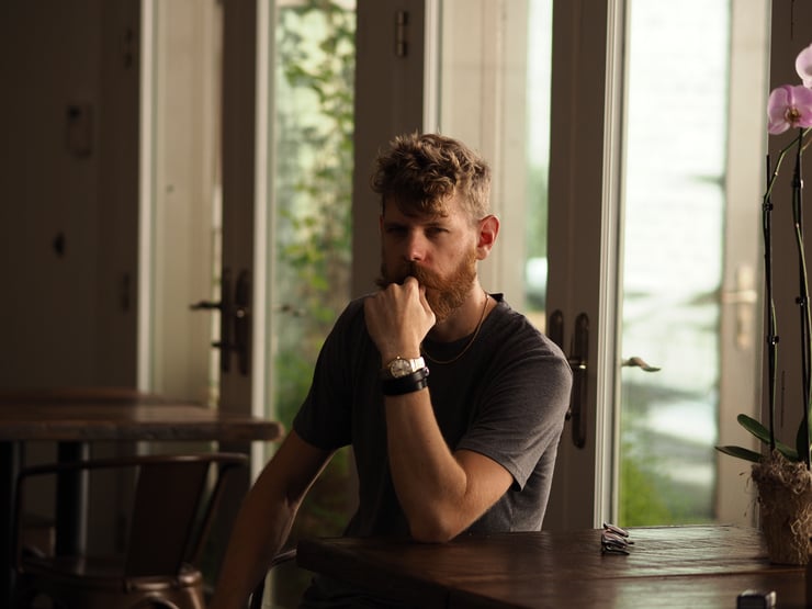 A sultry gentleman with a robust beard gazes in a dimly lit room.